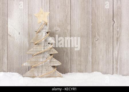 Shabby Chic in legno albero di Natale con spago garland in piedi nella neve contro un bianco sullo sfondo di legno Foto Stock