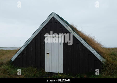 Piccola casa tradizionale triangolare con tetto d'erba con porta anteriore bianca, cieli sorvolati in campo aperto sull'isola di Flatey Breidafjordur Islanda Ovest Europa Foto Stock