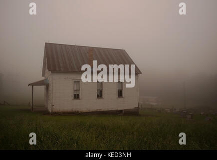 Abbandonate la chiesa di legno nella nebbia mattutina con il suo cimitero dietro di essa Foto Stock
