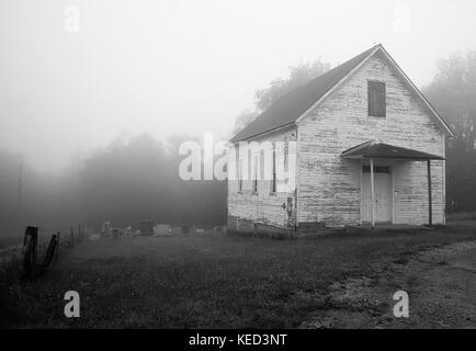 Abbandonate la chiesa di legno nella nebbia mattutina con il suo cimitero dietro di essa Foto Stock