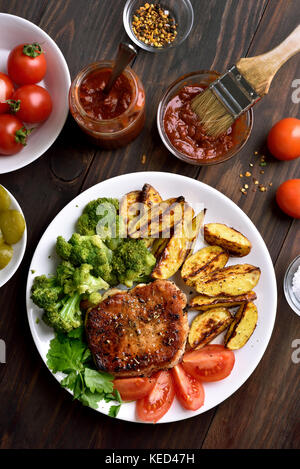 La carne fritta con broccoli, Spicchi di patate e le fette di pomodoro su sfondo di legno, vista dall'alto Foto Stock