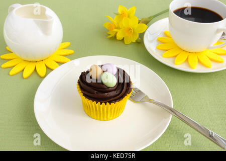 Composizione con la pasqua tortina di cioccolato decorate con le uova di pasqua, una tazza di caffè, latte il vaso e fiori di narciso sul verde sfondo a trama. Foto Stock