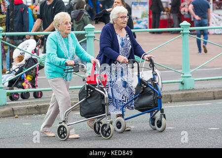 Donne anziane che attraversano una strada con camminatori su ruote a Brighton, East Sussex, Inghilterra, Regno Unito. Cornice Zimmer. Rullo. Tutti i giorni. Foto Stock