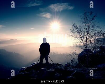 Fotografo prende foto di congelare autunnale di montagne, rocce ricoperte di polvere fresca neve. stony rock peak è aumentato da foggy valley. Foto Stock