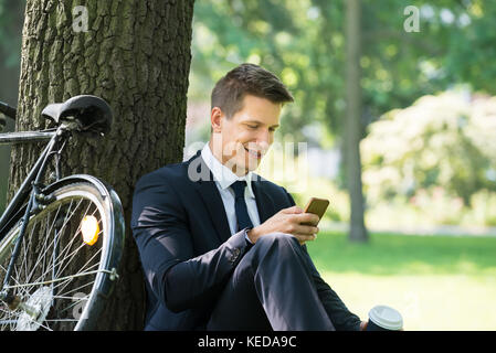 Felice giovane imprenditore maschio utilizzando il telefono cellulare in posizione di parcheggio Foto Stock