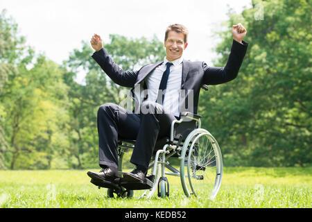 Felice giovane uomo disabili su sedia a rotelle con i bracci sollevati in posizione di parcheggio Foto Stock