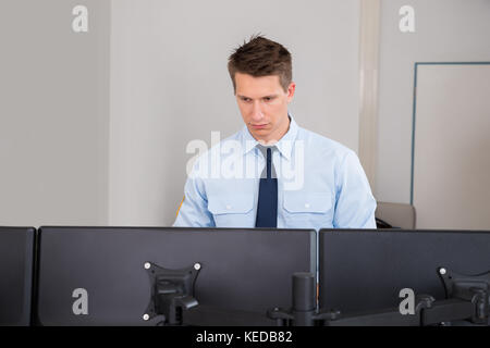 Giovane Maschio guardia di sicurezza in piedi di fronte a più computer in sala di controllo Foto Stock
