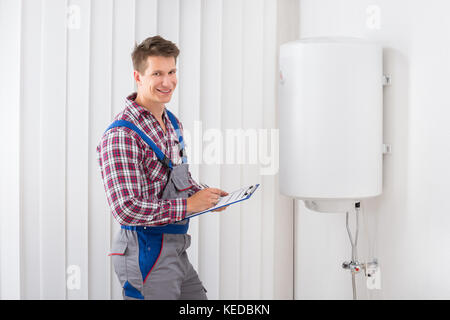 Giovane Maschio Plumber Holding appunti controllo Boiler elettrico Foto Stock