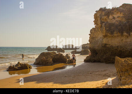 I vacanzieri sotto le rocce sedimentarie pietra arenaria scogliera sulla Praia da Oura Beach in Albuferia. Foto Stock