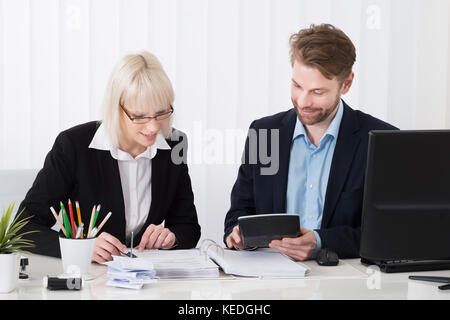 Due giovani imprenditori il calcolo delle fatture alla scrivania in ufficio Foto Stock