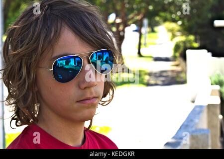 Giovane maschio adolescente indossando occhiali da sole blu colpo di testa contro sfondo suburbana. Foto Stock