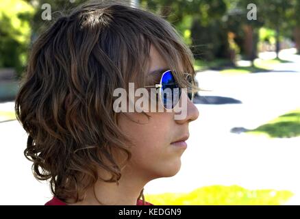 Giovane maschio adolescente indossando occhiali da sole blu colpo di testa contro sfondo suburbana. Foto Stock