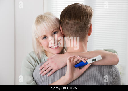 Felice giovane donna con test di gravidanza abbracciando l uomo a casa Foto Stock