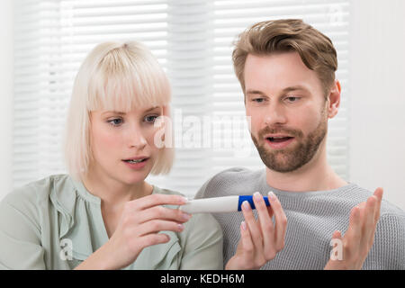 Close-up di scioccato giovane seduto sul divano guardando la gravidanza tester a home Foto Stock