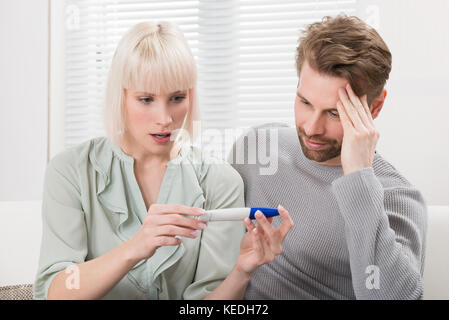 Close-up di scioccato giovane seduto sul divano guardando la gravidanza tester a home Foto Stock