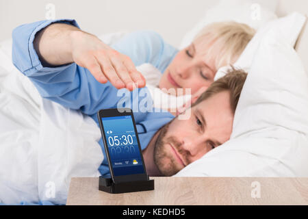 L'uomo sul letto del posticipo sveglia sul telefono cellulare schermo durante il sonno Foto Stock