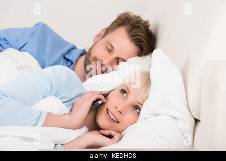 Donna che parla in privato sul cellulare mentre l uomo dorme nel letto di casa Foto Stock