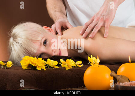 Sorridente giovane donna ricevere massaggio della spalla da un dispositivo massaggiatore in un centro di bellezza e benessere Foto Stock