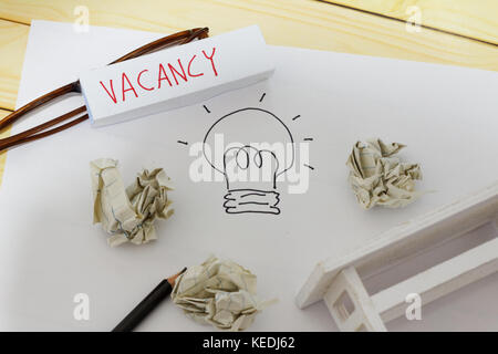 Posto vacante e concetto di occupazione. Libro bianco con il disegno di una lampadina, sgualciti papers, bicchieri, matita, mini toy tabella e parola vacante scritto su Foto Stock