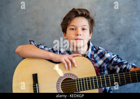 Ragazzo adolescente suonare la chitarra acustica contro la parete Foto Stock