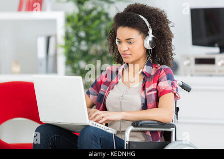 Giovane donna che utilizza un computer portatile mentre è seduto sulla sedia a rotelle Foto Stock