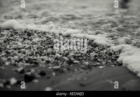 Lavaggio onde throguh conchiglie riempito beach Foto Stock