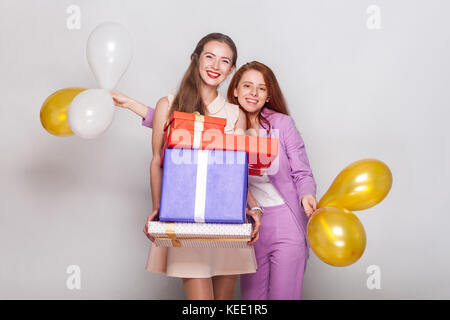 Due bellissima ragazza con regali box e pallone aerostatico hanno un aspetto della felicità e che mostra un segno v alla telecamera. studio shot Foto Stock