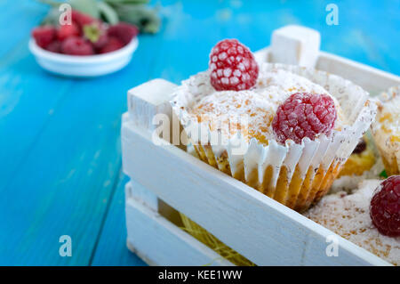 Torte di cagliata (Muffin) con lamponi, decorata con zucchero a velo. servire in un bianco scatola di legno. lamponi freschi in un vaso di ceramica. Foto Stock