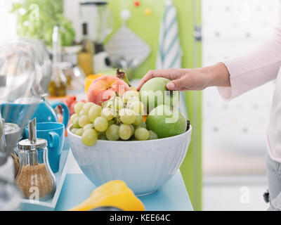 Donna prendendo una fresca mela verde da una coppa di frutta in cucina, nutrizione e cibo sano concetto Foto Stock