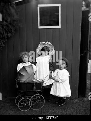 I bambini posano mentre giocano con un pram giocattolo da una capanna giardino c1900 fotografia di Tony Henshaw *** Local Caption *** dal negativo originale interamente posseduto. Foto Stock