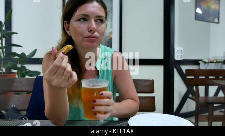 La ragazza è bere la birra nel bar. donna bevande birra e mangia pesce resto Foto Stock