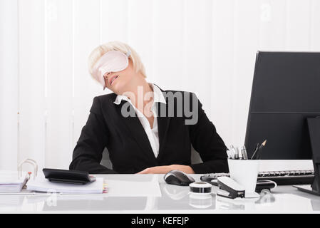 Giovane imprenditrice che indossa la maschera per gli occhi e il sonno in ufficio Foto Stock