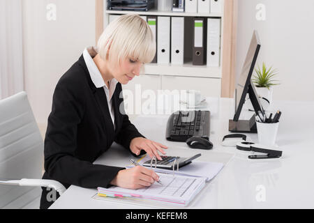 Giovani femmine contabile che lavora con la calcolatrice in Office Foto Stock