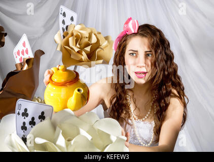 Giovane donna vestita come Alice nel Paese delle Meraviglie con grande bollitore e fiori Foto Stock