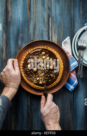 Noce italiano torta crostata con cioccolato e nocciole noce italiano torta crostata con cioccolato e nocciole e gli uomini con le mani in mano sono tagliati con un kni Foto Stock