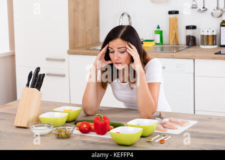 Giovane donna infelice in cucina vicino diverso ingrediente Foto Stock