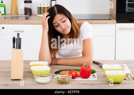 Giovane donna infelice in cucina vicino diverso ingrediente Foto Stock