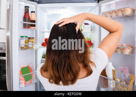 Vista posteriore del confuso donna alla ricerca di cibo nel frigo Foto Stock