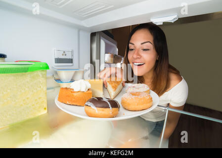 Giovane donna felice tenendo la fetta di torta dalla piastra in frigorifero Foto Stock