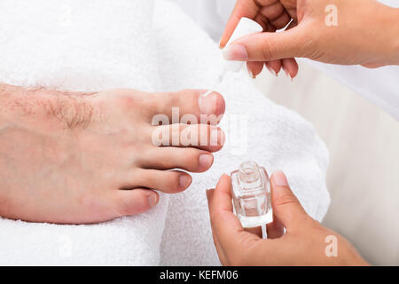 Close-up di un manicurist applicando idratante olio di chiodi sulla persona della toenail Foto Stock