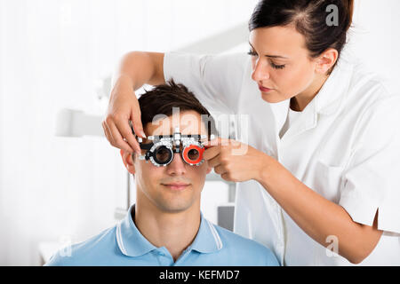 Giovani femmine all'ottico optometrista maschio di controllo paziente la visione con telaio di prova alla clinica oculistica Foto Stock