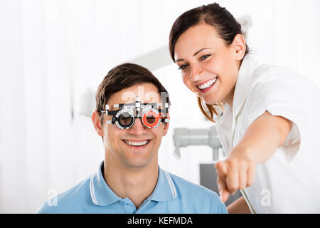Giovane donna sorridente all'ottico optometrista esame paziente la visione con telaio di prova Foto Stock