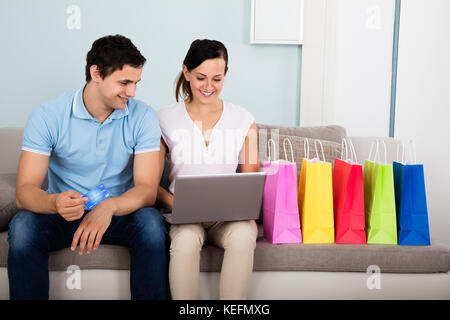 Giovane coppia felice shopping online con carta di credito seduto con le borse della spesa Foto Stock