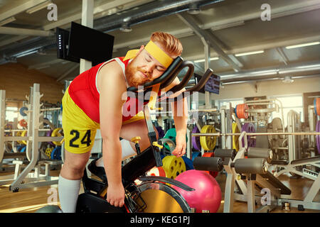 Un uomo grasso è stanco su un simulatore in palestra Foto Stock