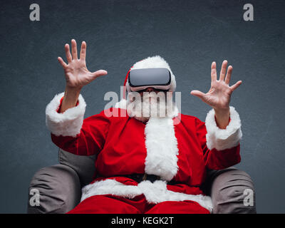 Santa Claus vivendo la realtà virtuale, indossa gli occhiali vr e di interazione con un ambiente virtuale Foto Stock