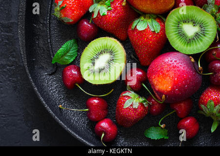 Estate succose fragole mature, ciliegia, kiwi e pesche su una piastra nera closeup. Foto Stock