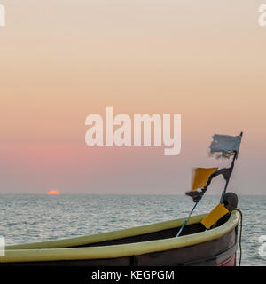 La parte superiore di una barca da pesca con le bandiere a prua. Il mare è dietro e il sole è appena una crescita di oltre l'orizzonte. Foto Stock