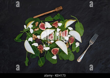 Insalata con le pere, baby spinaci, fichi, noci, formaggio di capra e miele sulla pietra nera di sfondo, vista dall'alto Foto Stock