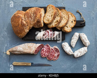 Vino set snack. italiano slami salsicce e pane rustico in legno scuro scheda sopra una ruvida grigio-blu sullo sfondo di calcestruzzo, vista dall'alto Foto Stock