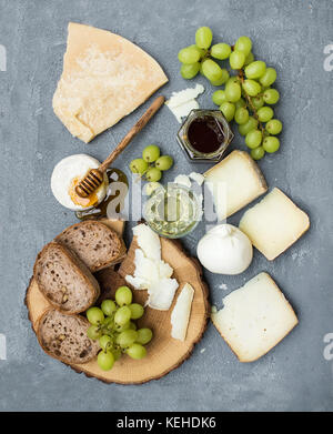 Antipasto di formaggio di selezione di vino o uno snack set. varietà di formaggi italiani, verde uva, le fette di pane e miele sulla rotonda di legno su cemento grigio Foto Stock
